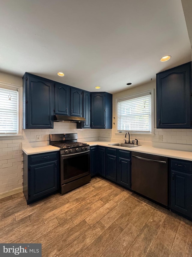 kitchen with under cabinet range hood, dishwashing machine, a sink, gas range, and light wood-style flooring