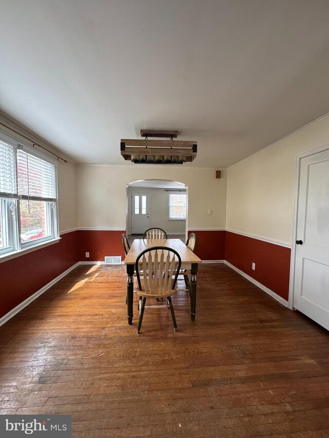 unfurnished dining area with visible vents, a wainscoted wall, wood finished floors, and arched walkways