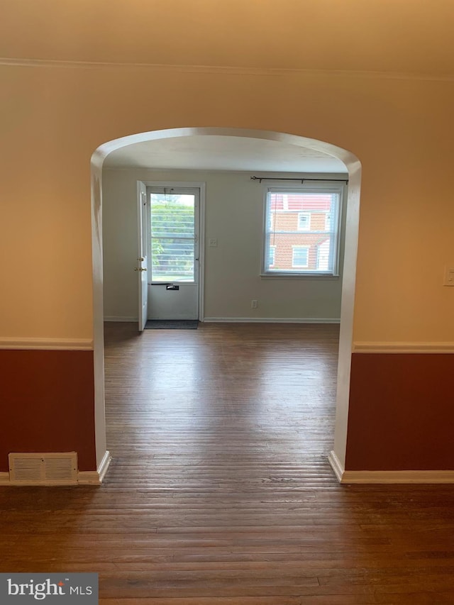 spare room with arched walkways, wood finished floors, visible vents, and baseboards