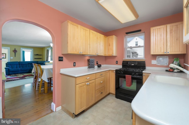 kitchen featuring black gas stove, a sink, arched walkways, and light brown cabinets