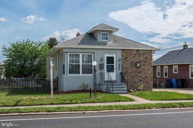 bungalow-style home featuring fence, a chimney, stucco siding, and a front lawn