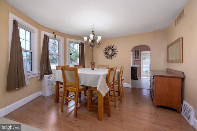 dining room featuring arched walkways, visible vents, a chandelier, and light wood finished floors