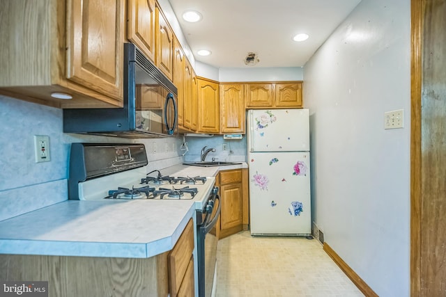 kitchen with black microwave, light countertops, brown cabinetry, freestanding refrigerator, and range with gas cooktop