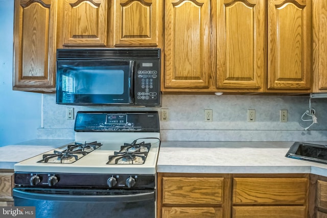 kitchen featuring light countertops, backsplash, black microwave, and range with gas cooktop