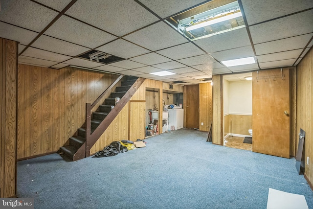 finished below grade area with wood walls, stairway, a paneled ceiling, washing machine and clothes dryer, and carpet