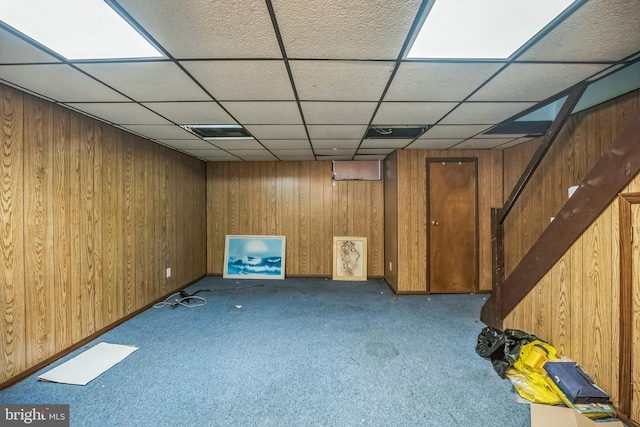 finished below grade area with visible vents, a paneled ceiling, wood walls, stairway, and carpet floors