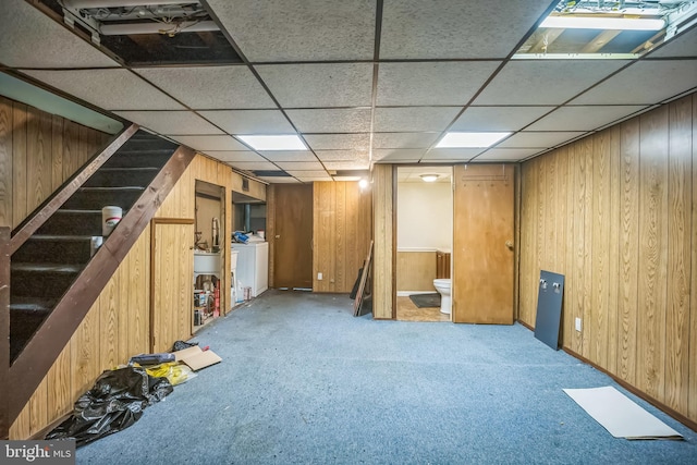 finished below grade area with washer / dryer, light carpet, wood walls, and stairs