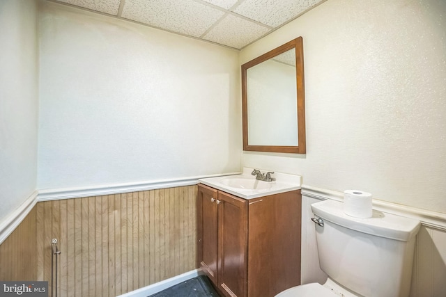 bathroom featuring vanity, a drop ceiling, toilet, and a wainscoted wall