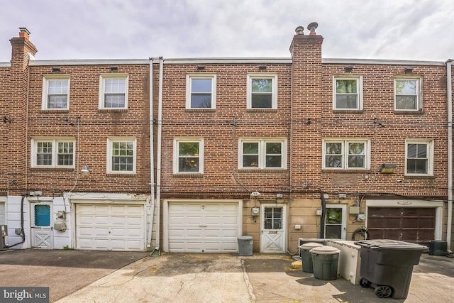 view of front of home featuring a garage, a chimney, driveway, and brick siding