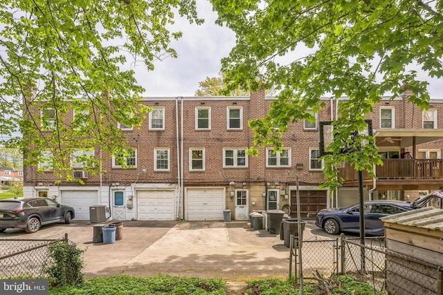 view of property with fence, an attached garage, driveway, and central AC unit