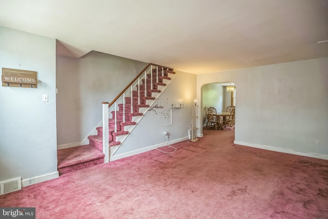 unfurnished living room with visible vents, arched walkways, stairs, and baseboards