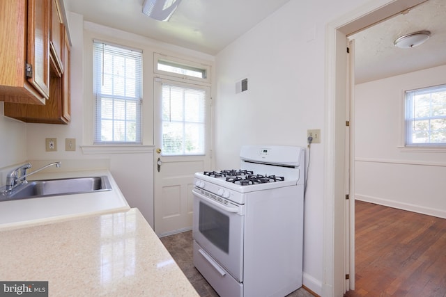 kitchen with brown cabinets, white range with gas stovetop, visible vents, and a sink
