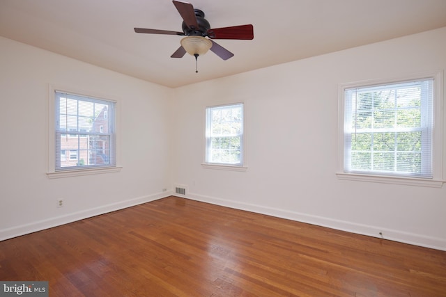 unfurnished room featuring a healthy amount of sunlight, visible vents, and wood finished floors