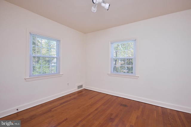 unfurnished room with a wealth of natural light, visible vents, baseboards, and wood finished floors