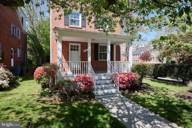 view of front of house featuring covered porch, brick siding, and a front yard