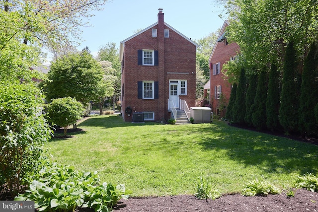rear view of house featuring a lawn, a chimney, brick siding, cooling unit, and entry steps