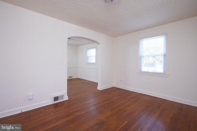 empty room featuring visible vents, dark wood-style flooring, baseboards, and arched walkways