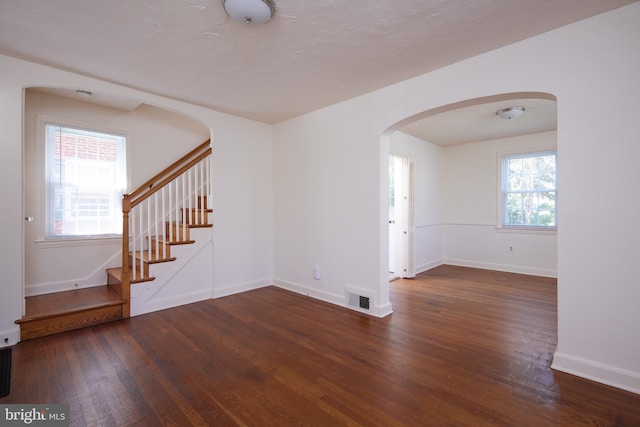 empty room featuring wood finished floors, visible vents, baseboards, arched walkways, and stairs