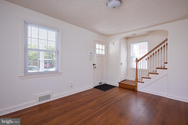 foyer entrance with visible vents, baseboards, dark wood-type flooring, and arched walkways