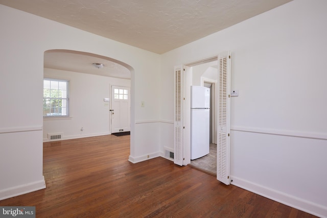 spare room with visible vents, wood finished floors, baseboards, and arched walkways
