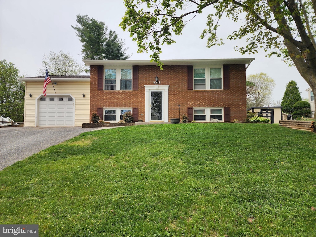 split foyer home with driveway, brick siding, a front yard, and a garage