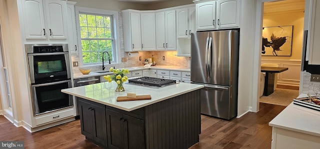 kitchen with a sink, white cabinets, decorative backsplash, dark wood finished floors, and appliances with stainless steel finishes