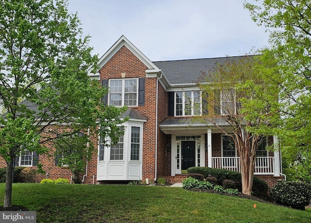 traditional-style home featuring brick siding, a shingled roof, a front lawn, and covered porch