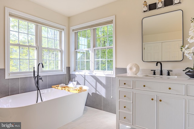 bathroom featuring vanity, plenty of natural light, a freestanding bath, and tile walls
