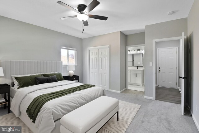 bedroom featuring light colored carpet, a ceiling fan, baseboards, ensuite bathroom, and a closet