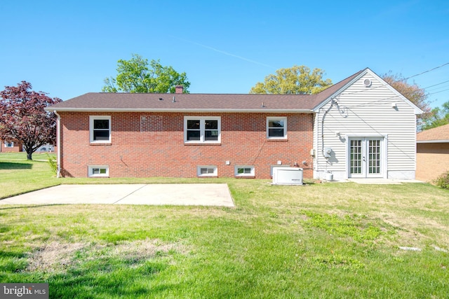 back of property with brick siding, a chimney, a patio area, french doors, and a lawn