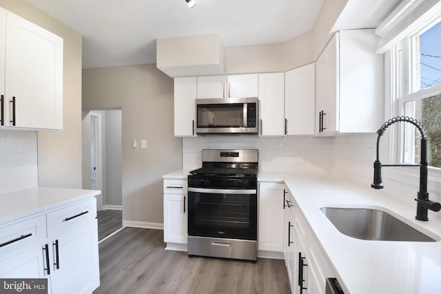 kitchen with a sink, light wood-style floors, light countertops, stainless steel appliances, and tasteful backsplash