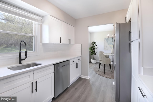 kitchen with white cabinets, a sink, light wood finished floors, stainless steel appliances, and backsplash