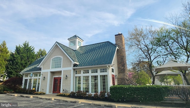 view of front of house with metal roof, a standing seam roof, a chimney, and uncovered parking