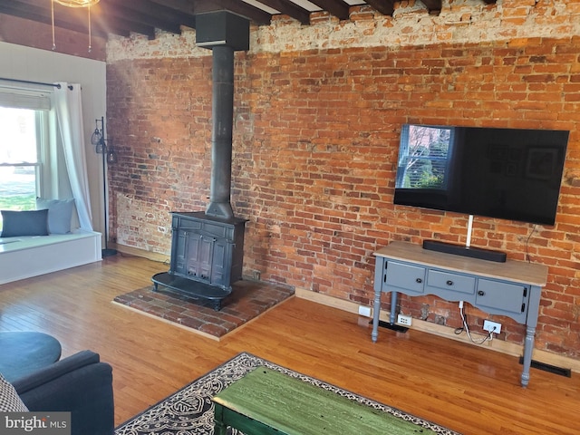 living room with beamed ceiling, a wood stove, baseboards, brick wall, and wood finished floors