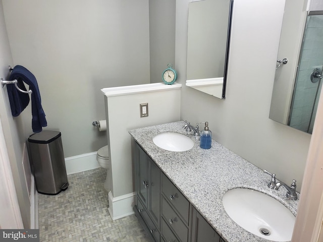 bathroom featuring double vanity, toilet, baseboards, and a sink