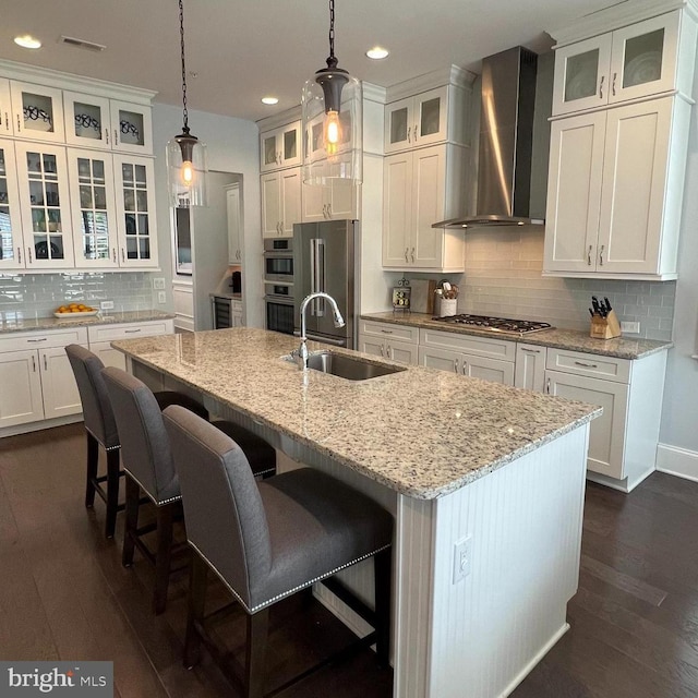 kitchen featuring wall chimney range hood, decorative backsplash, visible vents, appliances with stainless steel finishes, and a sink