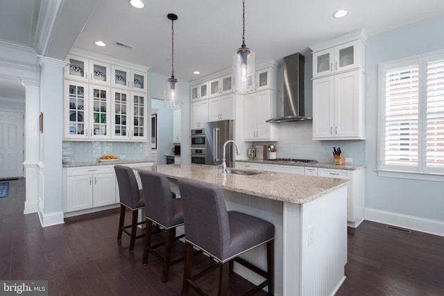 kitchen with a sink, wall chimney exhaust hood, white cabinetry, baseboards, and decorative backsplash