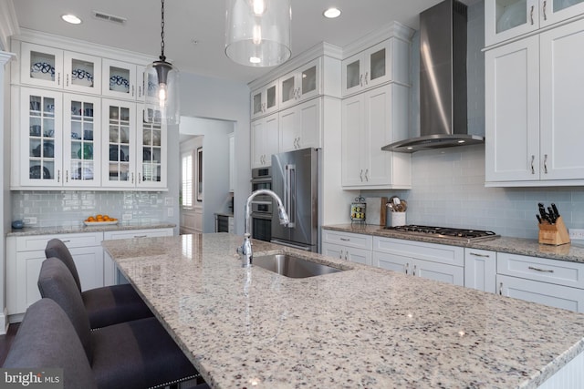 kitchen with white cabinets, an island with sink, wall chimney exhaust hood, stainless steel appliances, and visible vents