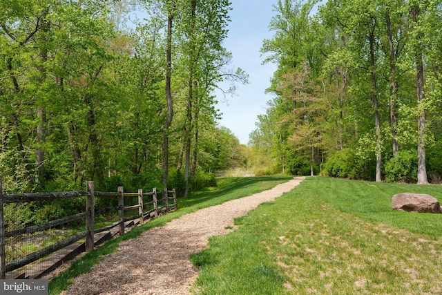view of property's community with a lawn, fence, and a forest view