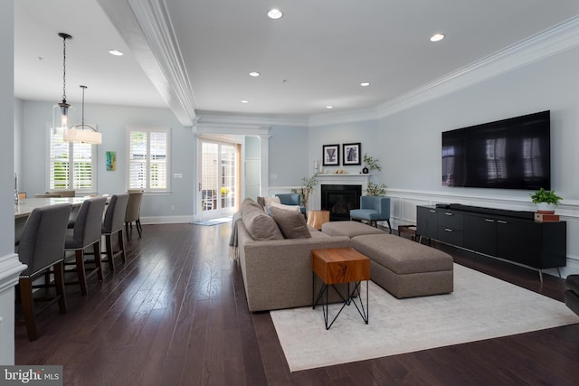 living area with crown molding, a glass covered fireplace, recessed lighting, baseboards, and dark wood-style floors