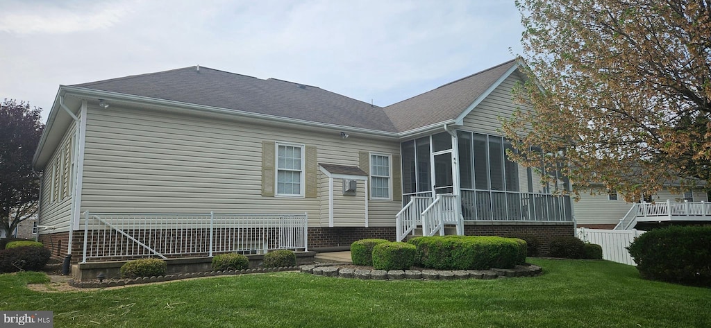 rear view of property with a yard, a sunroom, a shingled roof, and fence