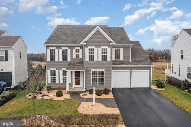 colonial inspired home with an attached garage, roof with shingles, a front yard, and aphalt driveway