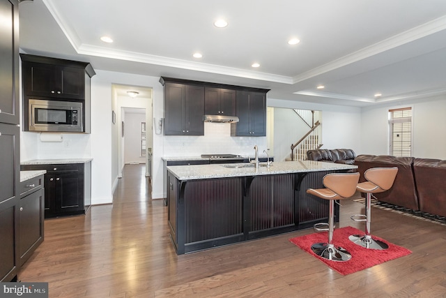 kitchen featuring stainless steel microwave, open floor plan, a breakfast bar area, and a raised ceiling