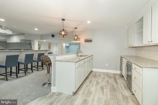 kitchen with white cabinets, a sink, baseboards, a peninsula, and light wood-style flooring