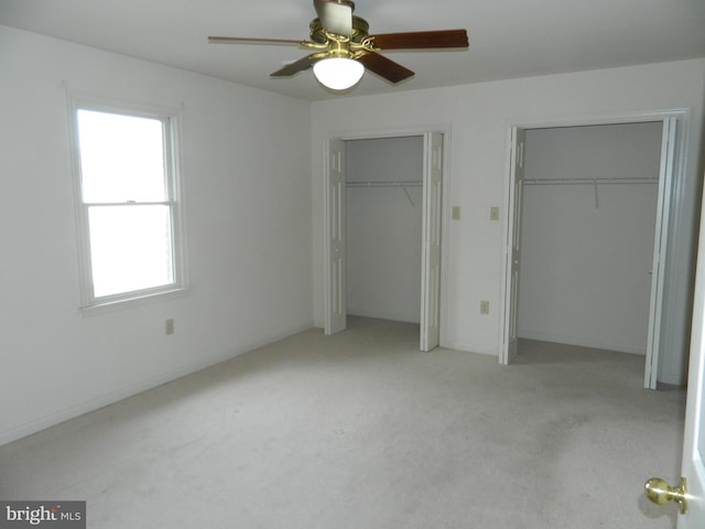 unfurnished bedroom with light carpet, two closets, and ceiling fan