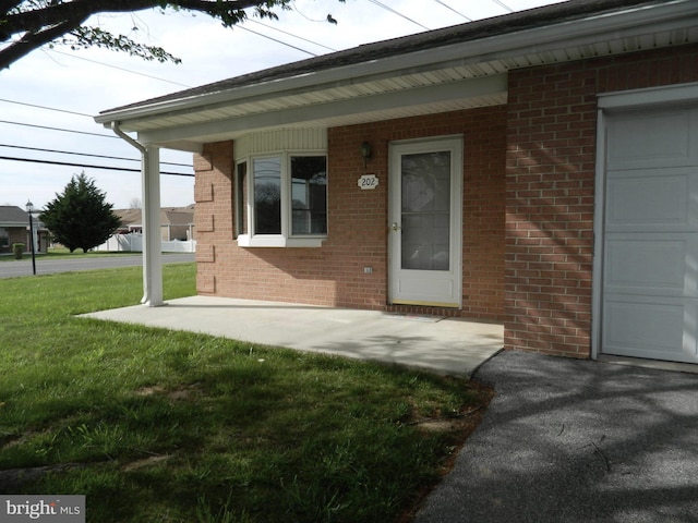 doorway to property with brick siding, a yard, and a garage