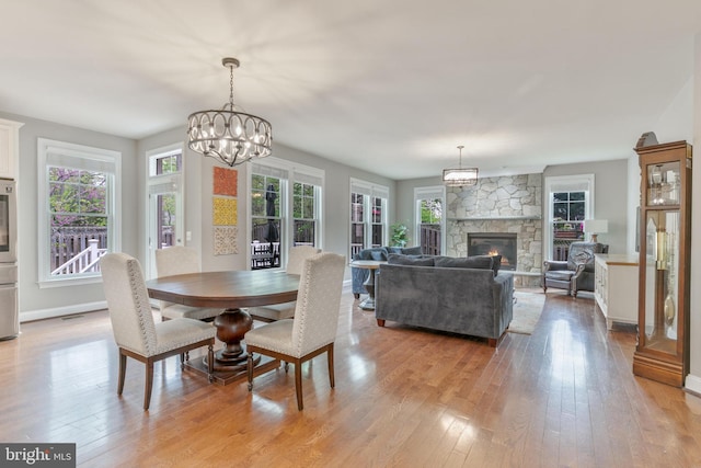 dining room with light wood finished floors, baseboards, a fireplace, and a notable chandelier