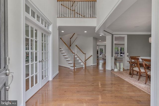 foyer featuring stairway, french doors, light wood finished floors, baseboards, and ornamental molding