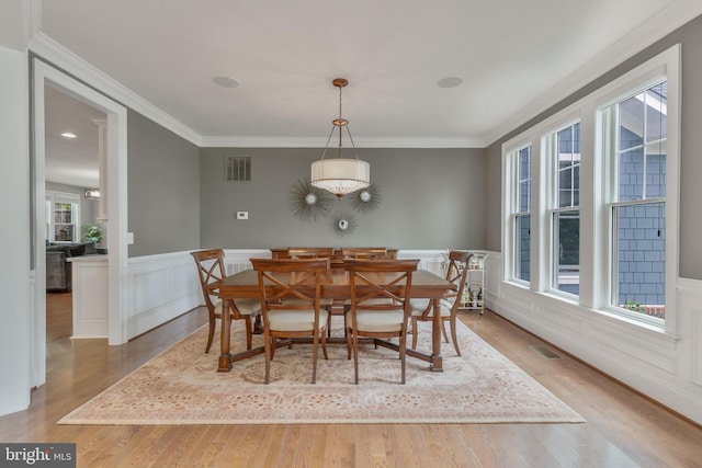 dining room featuring wainscoting, wood finished floors, visible vents, and crown molding