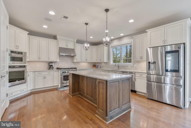 kitchen featuring under cabinet range hood, appliances with stainless steel finishes, a chandelier, and white cabinetry